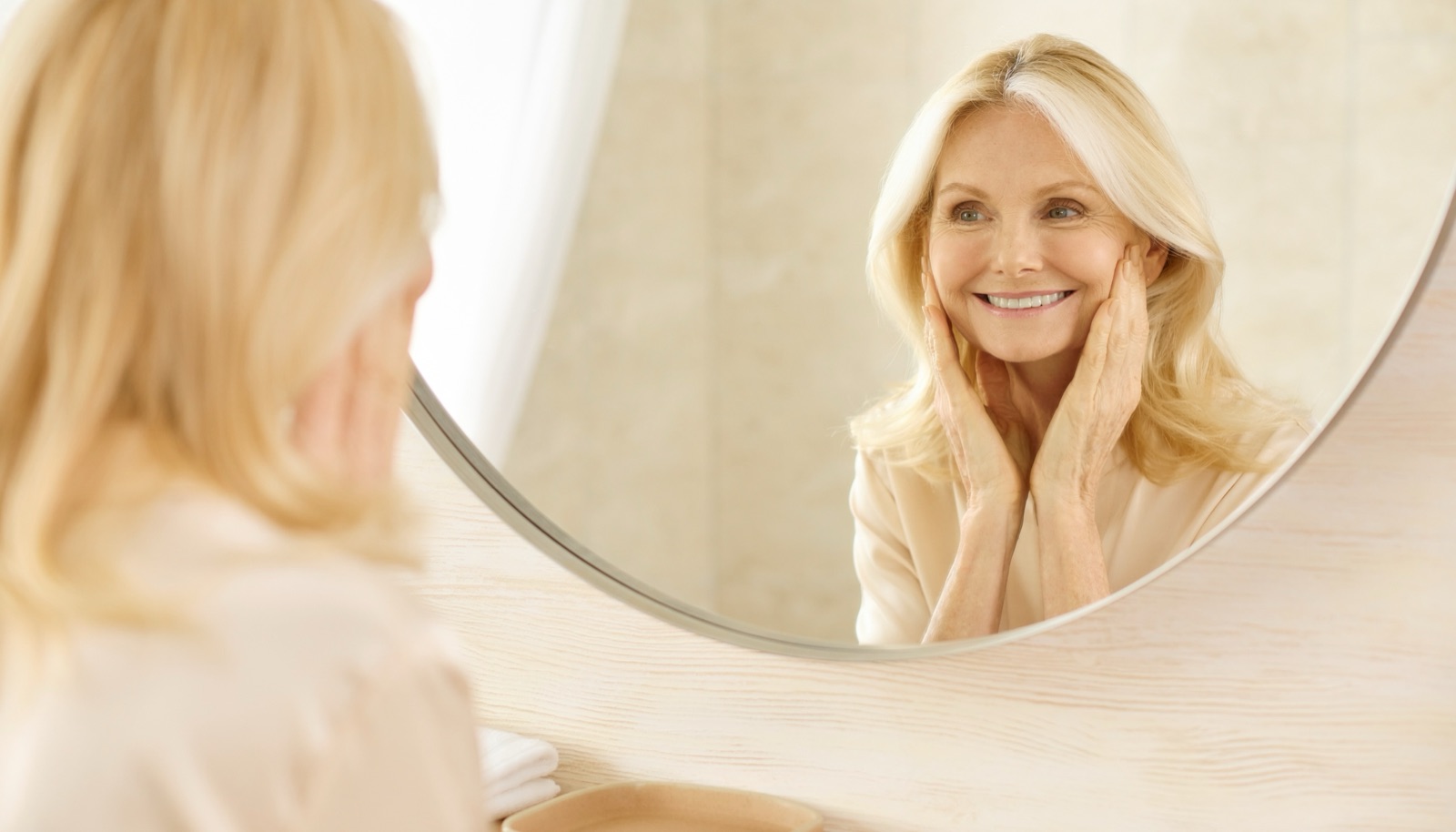 Woman smiling at her reflection in a bathroom mirror