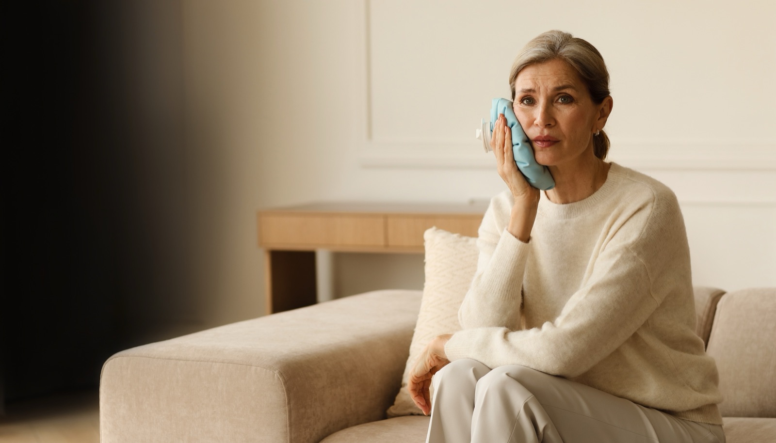 Woman holding a cold compress to her cheek on the couch
